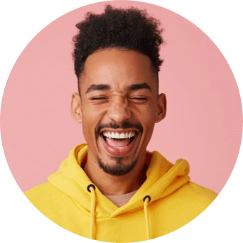 Un hombre con una sudadera amarilla con capucha sonríe ampliamente mientras cierra los ojos.