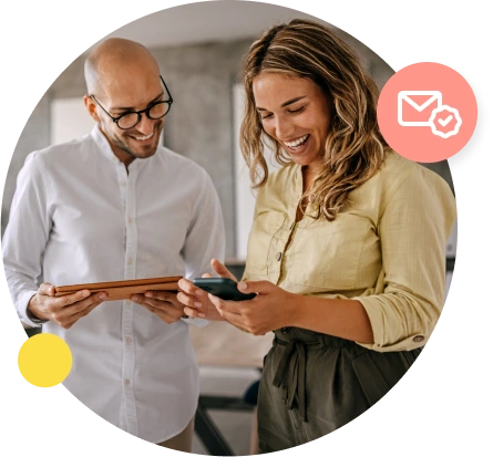 A man in a white shirt holds his tablet and looks over at a phone held by his female coworker.
