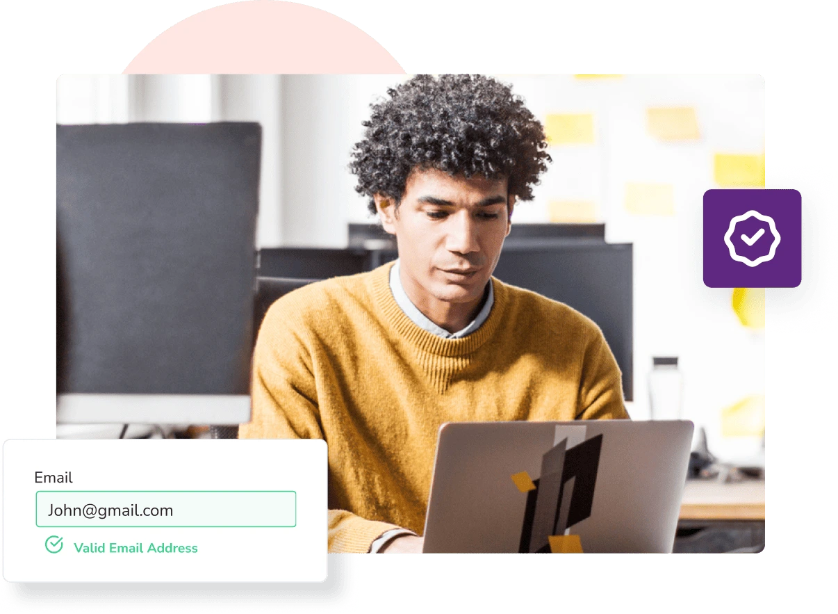A man in an orange jumper sits in an office and types on his laptop to check if 'john@gmail.com' is a valid email address.