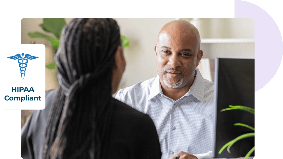Man and woman sit across from each other at a desk to discuss email security accompanied by a HIPAA-compliant logo.