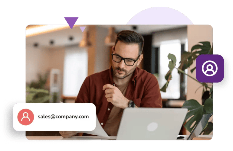 A man with glasses and a brown shirt looks at a sheet of paper next to his laptop and the email address 'sales@company.com.'