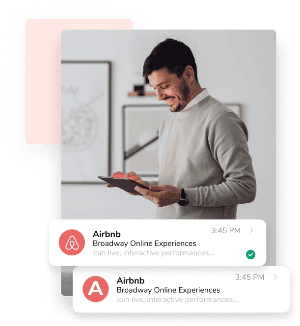 A man in a beige sweater smiles and looks down at the tablet he's holding, while two emails from Airbnb sit in front of him.