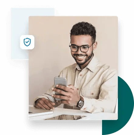 Hombre sentado en un escritorio sonriendo mientras usa la validación de correo electrónico ZeroBounce en su teléfono móvil.