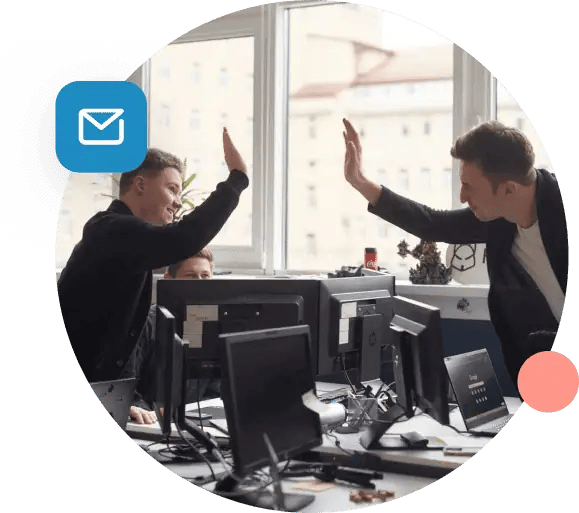 Two men reaching over their desks to high five.