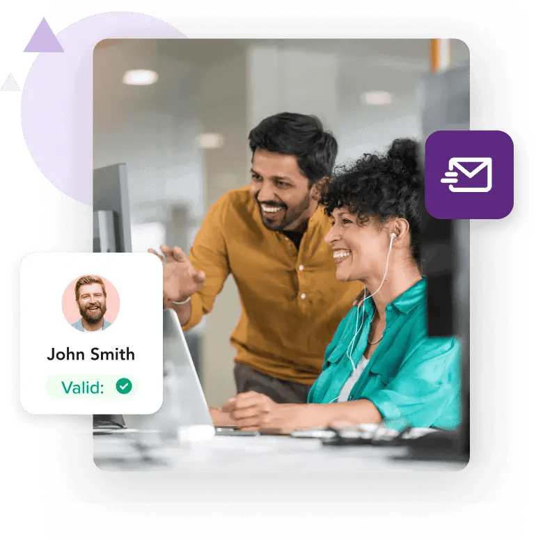 A woman seated at her desk and a man standing next to her smile while looking at a computer screen alongside a profile for ‘John Smith’ with a ‘Valid’ message.