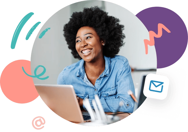 Picture of young woman wearing blue denim shirt working in front of computer and smiling about the celebration of National Email Day on April 23