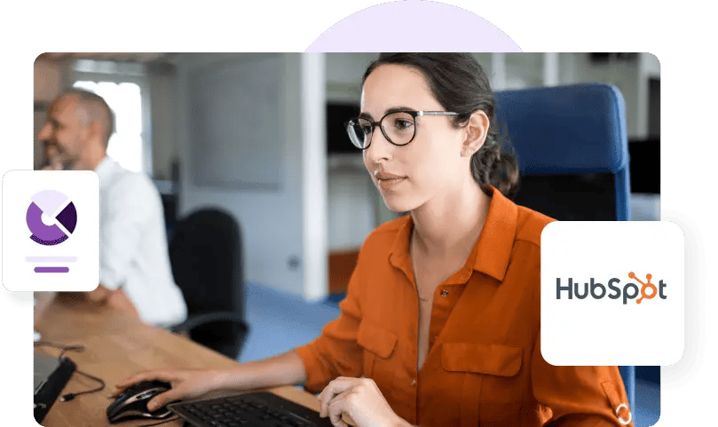 A woman in an orange shirt and glasses holds a mouse and looks at her monitor next to a HubSpot logo.