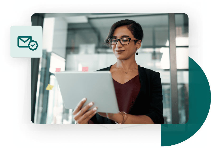 Casual businesswoman stands in front of a glass wall and works from her tablet next to a valid email icon