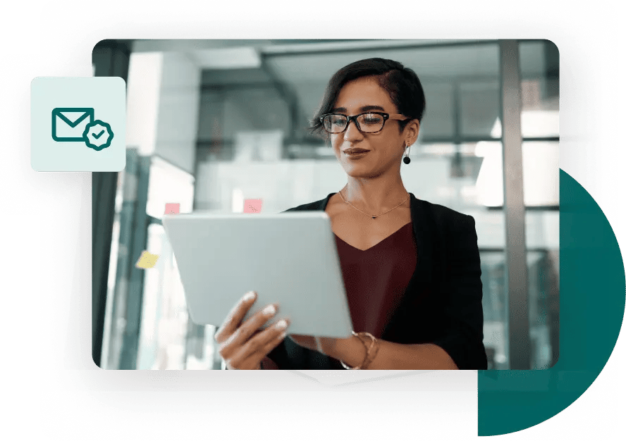 Casual businesswoman stands in front of a glass wall and works from her tablet next to a valid email icon