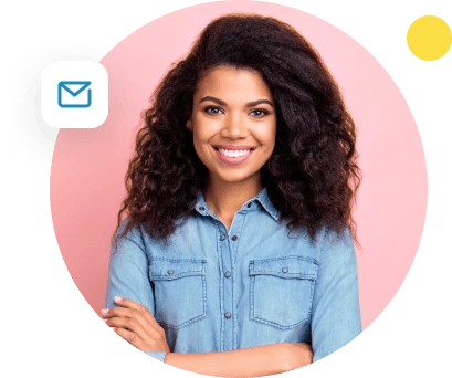 A woman wearing denim smiles at the camera in front of a pink background.