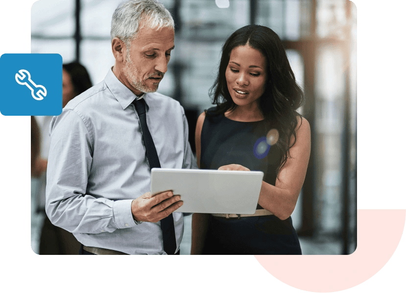 An older man in a shirt and tie and a woman in a dark dress discuss what’s on the tablet they’re holding.