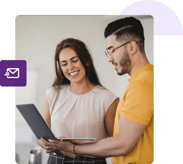 Un hombre sostiene su computadora portátil y muestra su pantalla a una mujer a su lado que está sonriendo.