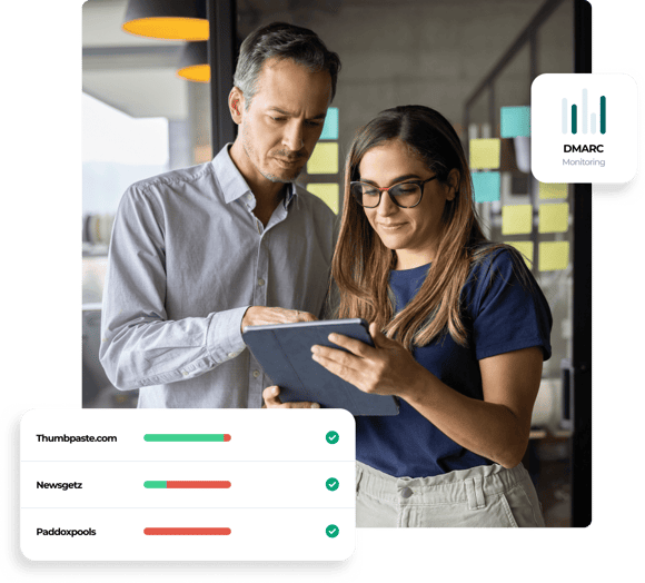 A man in a dress shirt stands next to a woman in casual wear and points at the tablet she’s holding, which shows DMARC compliance reports for 3 email domains.