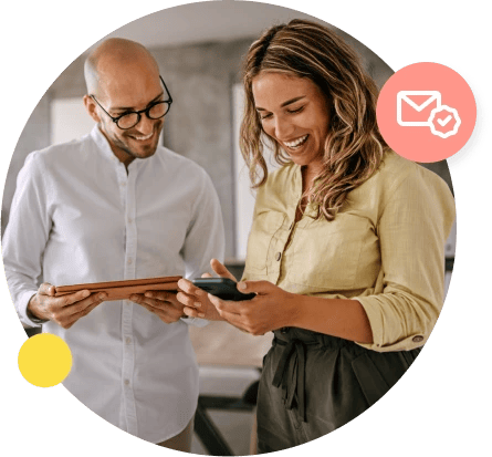 A man in a white shirt holds his tablet and looks over at a phone held by his female coworker.