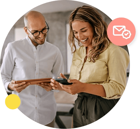A man in a white shirt holds his tablet and looks over at a phone held by his female coworker.