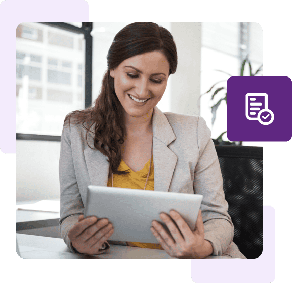 A woman wearing a blazer smiles as she looks down at her tablet.