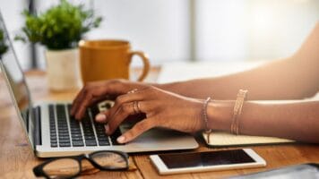 Hands type on keyboard with coffee mug in foreground as email user consider the AI ramifications of Gemini's use in Gmail.
