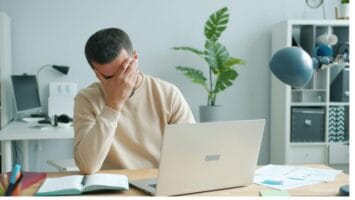 Young man puts his hand on his face in anguish due to email fatigue.