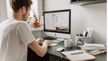 Young man sits before computer with notebook and coffee cup as he learns about catch-all vs invalid emails.