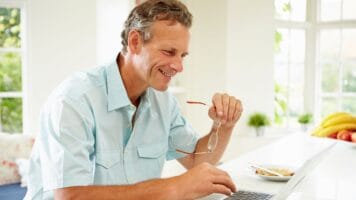 Middle aged man holds eyeglasses while avoiding email phrases that make him seem less confident.