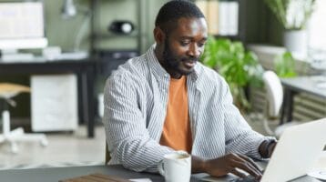 Man wearing light grey shirt writing email at computer to convince boss he needs ZeroBounce email validation tools