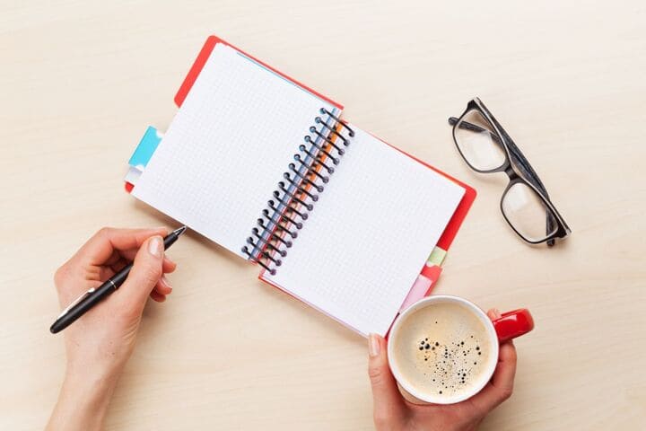 Image of a hand with coffee and a notebook. 