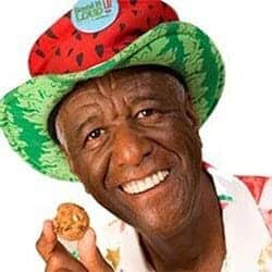 Entrepreneur Wally Amos holds a cookie in his hand while wearing a colorful watermelon hat.