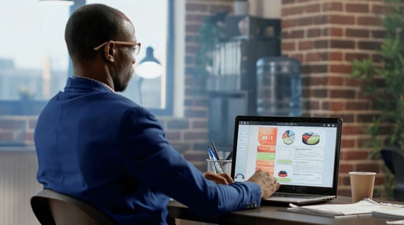 Man seated at computer sends prospecting email in well lit room.