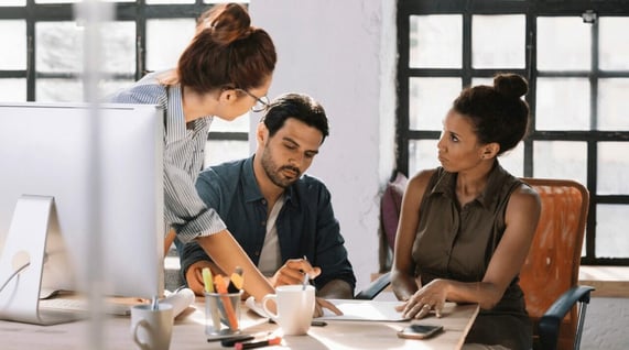 Three work colleagues discuss spam email checker strategies in front of a computer.