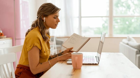 Young woman holding a notebook and working on her computer writing a media pitch email