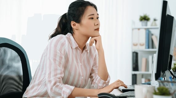 Young Asian woman sitting at desk and working at computer, learning about the difference between a hard vs soft bounce in email marketing