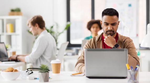 Young man working at computer in an office with two other colleagues behind, running an email blacklist check for email deliverability