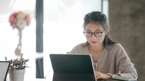 Bespectacled Asian woman sits at her laptop and uses the ZeroBounce Email Finder service.