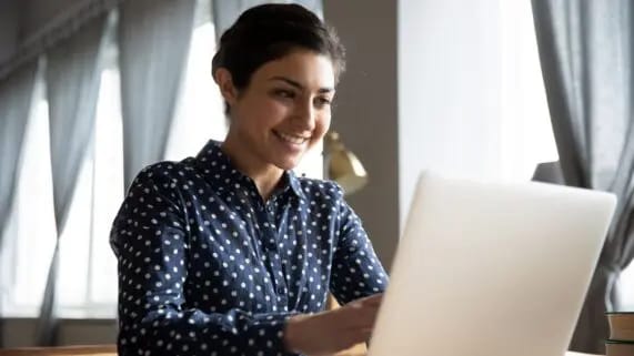 Young woman in patterned shirt sits in front of laptop to view her Mailchimp dashboard.